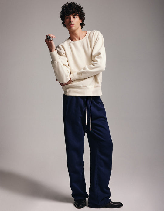Text on image says "Shop crewnecks made for him" - Image of a man standing wearing an ivory crewneck and Navy cotton pant with gold eyelets and drawstrings.