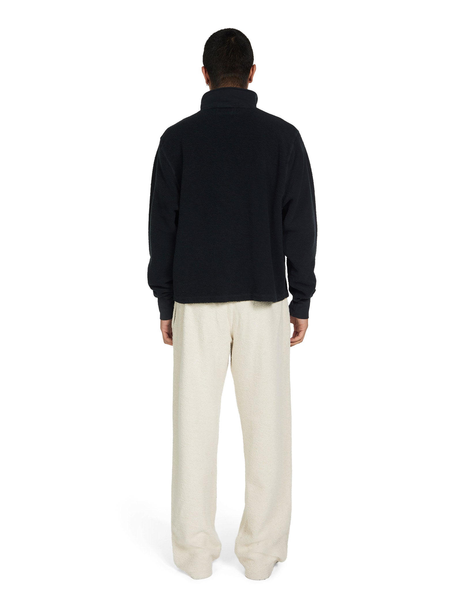 Person wearing a black sweater and ivory pants on a white background